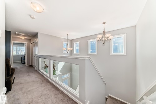 Upper-level landing featuring a glass panel railing, carpeted flooring, and a decorative chandelier - 267 Sturtz Bend, Leduc, AB - Indoor Photo Showing Other Room