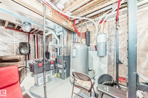 Unfinished basement space featuring exposed ceiling joists, insulation, and visible utility lines, with a water heater and furnace unit present - 267 Sturtz Bend, Leduc, AB - Indoor Photo Showing Basement