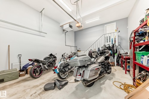 Spacious garage featuring a concrete floor, built-in shelving, overhead lighting, an interior staircase, and a dedicated entry door - 267 Sturtz Bend, Leduc, AB - Indoor Photo Showing Garage
