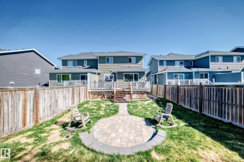 Expansive backyard featuring a circular paver patio with stone border, private wood fencing, and a tiered wooden deck with white railing - 267 Sturtz Bend, Leduc, AB - Outdoor With Deck Patio Veranda