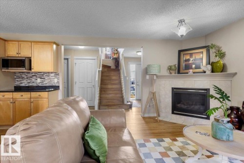 Living area featuring a tiled fireplace with mantel, recessed fireplace insert, and a built-in kitchen counter with wood cabinetry, dark countertops, and a tiled backsplash - 3356 25 Ave, Edmonton, AB - Indoor Photo Showing Living Room With Fireplace