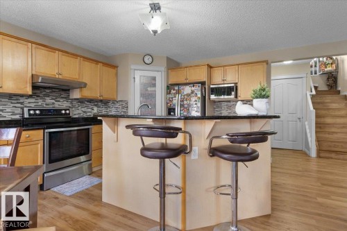 Kitchen featuring light wood cabinetry, dark countertops, and a mosaic tile backsplash - 3356 25 Ave, Edmonton, AB - Indoor Photo Showing Kitchen With Stainless Steel Kitchen