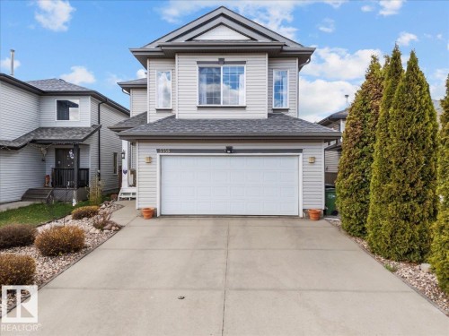 Two-story property featuring light gray horizontal siding, a prominent attached two-car garage with a white panel door, and a concrete driveway - 3356 25 Ave, Edmonton, AB - Outdoor With Facade
