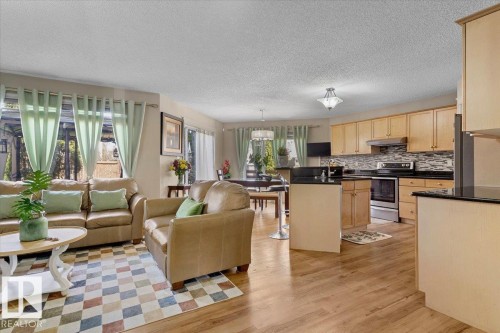 Open-concept living area featuring wood-finish flooring, a kitchen with light wood cabinetry and dark countertops, stainless steel appliances, and a tiled backsplash - 3356 25 Ave, Edmonton, AB - Indoor