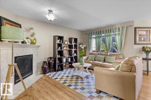 Living area featuring a fireplace with a tiled surround and mantle, wood-finish flooring, a ceiling-mounted light fixture, large windows, and built-in shelving - 3356 25 Ave, Edmonton, AB - Indoor Photo Showing Living Room With Fireplace
