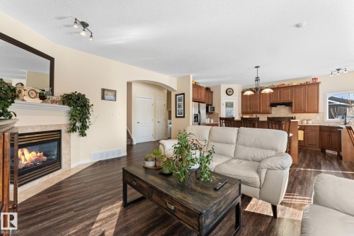 Open-concept living space with dark wood-finish flooring, a built-in fireplace featuring a tile surround and mantel, and an arched entry - 112 Lakeland Point(E), Beaumont, AB - Indoor Photo Showing Living Room With Fireplace
