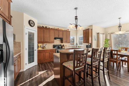 Kitchen featuring wood-finish flooring, warm-toned cabinetry, stainless steel refrigerator, and a kitchen island with bar seating - 112 Lakeland Point(E), Beaumont, AB - Indoor
