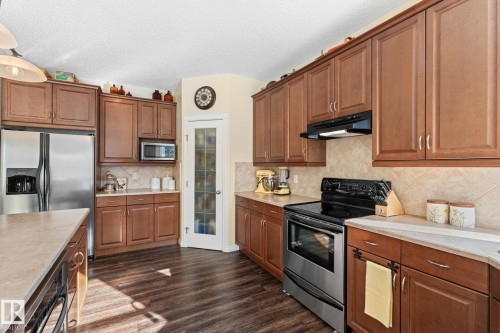 Kitchen featuring extensive wood cabinetry, stone-finish countertops, stainless steel appliances, and wood-finish flooring - 112 Lakeland Point(E), Beaumont, AB - Indoor Photo Showing Kitchen