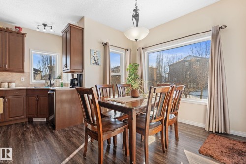 Dining area featuring expansive windows, wood-finish flooring, and a contemporary chandelier - 112 Lakeland Point(E), Beaumont, AB - Indoor Photo Showing Dining Room