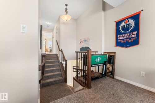 Carpeted staircase featuring a dark wood handrail and balusters, leading to an upper-level hallway with a decorative pendant light fixture - 112 Lakeland Point(E), Beaumont, AB - Indoor Photo Showing Other Room