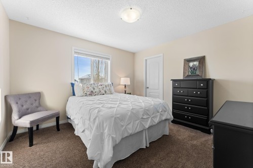 Room featuring a window with white trim, light beige wall paint, textured brown carpeting, and a white interior door - 112 Lakeland Point(E), Beaumont, AB - Indoor Photo Showing Bedroom