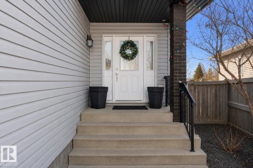 Inviting front entry featuring a white door with sidelights, a dark brick pillar, a black handrail, and concrete steps - 112 Lakeland Point(E), Beaumont, AB - Outdoor With Exterior