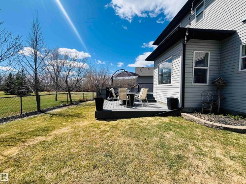 Expansive backyard with a manicured lawn, featuring a spacious composite deck with railing, black chain-link fencing, and mature trees - 112 Lakeland Point(E), Beaumont, AB - Outdoor