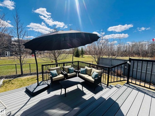 Spacious composite deck with black metal railings, offering an expansive backyard with mature trees and a chain-link fence - 112 Lakeland Point(E), Beaumont, AB - Outdoor With Deck Patio Veranda