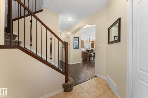 Entryway featuring ceramic tile flooring, a carpeted staircase with wood handrail and wrought iron spindles, and an arched doorway leading to wood-finish flooring - 112 Lakeland Point(E), Beaumont, AB - Indoor Photo Showing Other Room