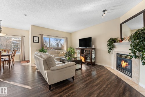 Inviting living space featuring wood-finish flooring, a tiled fireplace with a mantel, and track lighting - 112 Lakeland Point(E), Beaumont, AB - Indoor Photo Showing Living Room With Fireplace