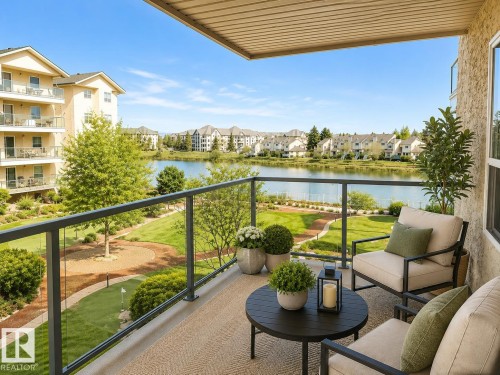 Private balcony with glass panel railing overlooking a landscaped green space and a serene body of water - 219 9535 176 Street, Edmonton, AB - Outdoor With Body Of Water With View With Exterior