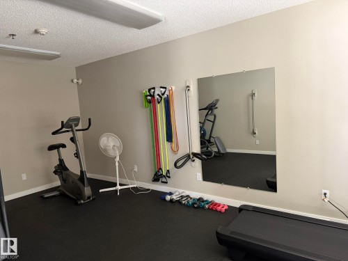 Dedicated fitness room featuring rubberized flooring and a large wall-mounted mirror - 219 9535 176 Street, Edmonton, AB - Indoor Photo Showing Gym Room