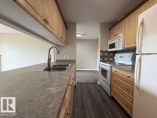 Kitchen featuring wood-finish cabinetry, a double basin stainless steel sink with a gooseneck faucet, an electric range with an overhead microwave, and wood-look flooring - 316 16303 95 Street, Edmonton, AB - Indoor Photo Showing Kitchen With Double Sink