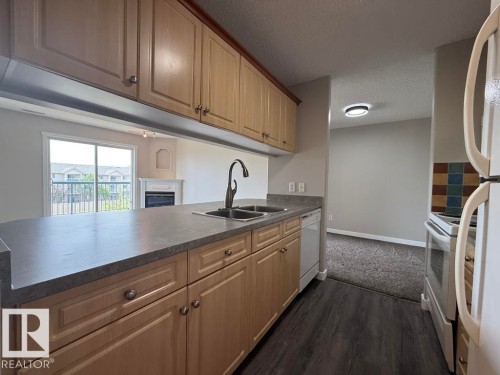 Kitchen featuring light wood-finish cabinetry, a dual basin sink with a gooseneck faucet, a white dishwasher, and dark wood-finish flooring - 316 16303 95 Street, Edmonton, AB - Indoor Photo Showing Kitchen