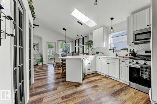 White kitchen featuring shaker-style cabinetry, stainless steel appliances, a tile backsplash, wood-finish flooring, and a large skylight - 3208 135A Avenue, Edmonton, AB - Indoor Photo Showing Kitchen With Upgraded Kitchen