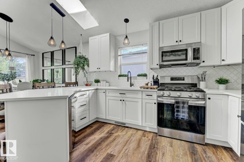 Contemporary kitchen featuring white shaker cabinetry, stainless steel appliances, a white solid surface countertop, and wood-finish flooring - 3208 135A Avenue, Edmonton, AB - Indoor Photo Showing Kitchen With Upgraded Kitchen