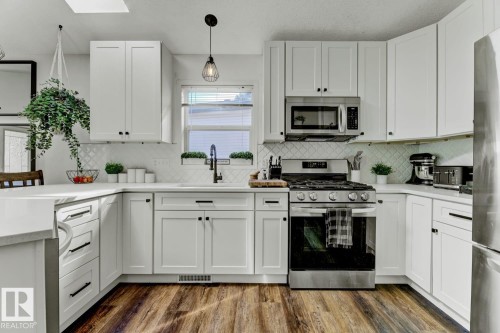 Kitchen featuring white shaker-style cabinetry, stainless steel appliances, wood-finish flooring, white diamond-patterned backsplash, and light-colored countertops - 3208 135A Avenue, Edmonton, AB - Indoor Photo Showing Kitchen