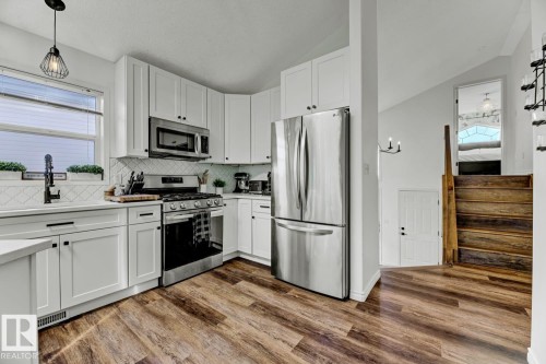 Modern kitchen featuring white shaker cabinetry, stainless steel appliances, a tile backsplash, and wood-finish flooring - 3208 135A Avenue, Edmonton, AB - Indoor Photo Showing Kitchen With Stainless Steel Kitchen