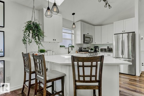 Kitchen featuring a peninsula with a light-toned countertop, white cabinetry, a tiled backsplash, stainless steel appliances, and wood-finish flooring - 3208 135A Avenue, Edmonton, AB - Indoor Photo Showing Kitchen With Stainless Steel Kitchen