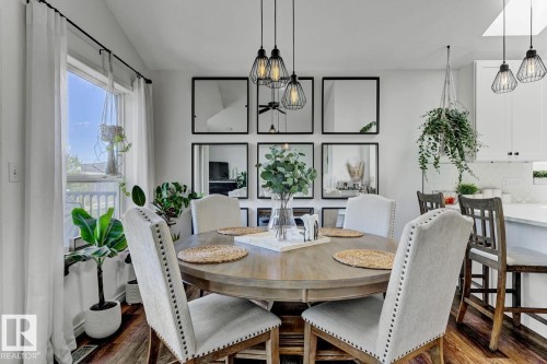 Dining area featuring wood-finish flooring, a contemporary chandelier with three wire-frame pendants, white walls, and a window with white sheer curtains - 3208 135A Avenue, Edmonton, AB - Indoor Photo Showing Dining Room