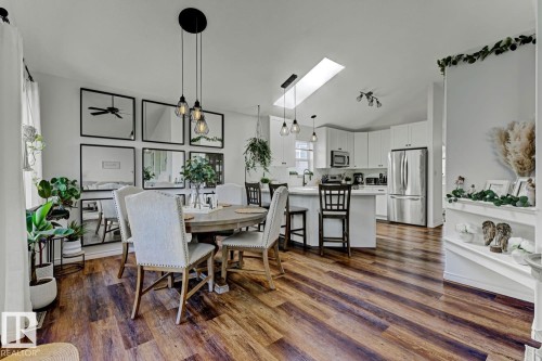 Open-concept living space featuring wood-finish flooring, a contemporary kitchen with white cabinetry, stainless steel appliances, a kitchen island with seating, a skylight, and a dining area illuminated by pendant lighting - 3208 135A Avenue, Edmonton, AB - Indoor Photo Showing Dining Room