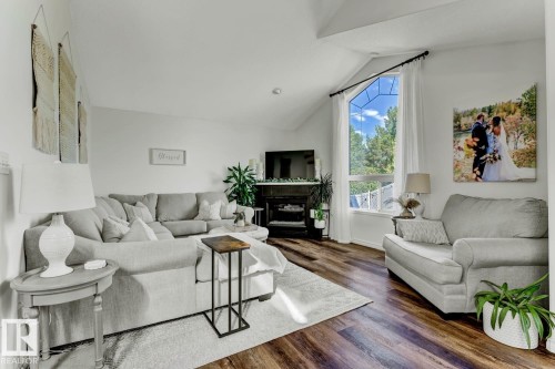Living area featuring vaulted ceilings, wood-finish flooring, a large corner window, and a built-in electric fireplace - 3208 135A Avenue, Edmonton, AB - Indoor Photo Showing Living Room
