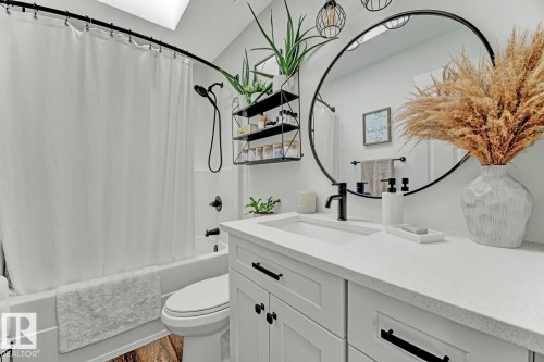 Bathroom featuring a white vanity with shaker-style cabinetry, a solid surface countertop, an undermount sink, and matte black fixtures - 3208 135A Avenue, Edmonton, AB - Indoor Photo Showing Bathroom