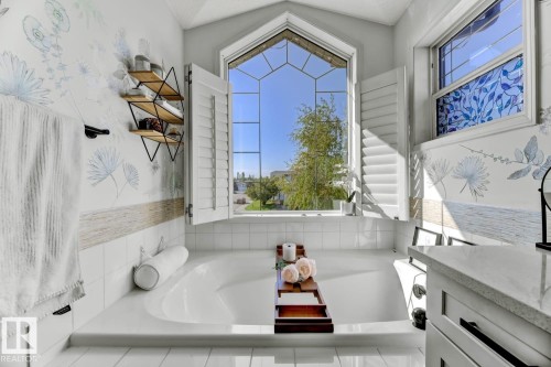 Deep soaking tub with a unique arched window featuring geometric muntins and white plantation shutters - 3208 135A Avenue, Edmonton, AB - Indoor Photo Showing Bathroom