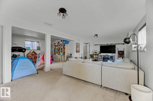 Expansive carpeted room featuring a ceiling-mounted light fixture and recessed ceiling lighting - 3208 135A Avenue, Edmonton, AB - Indoor