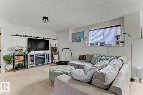 Spacious living area featuring light-colored carpeting, a large window with blinds, and a dedicated media console with an integrated electric fireplace - 3208 135A Avenue, Edmonton, AB - Indoor Photo Showing Living Room