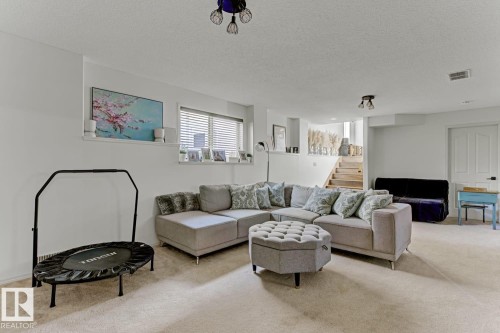 Carpeted lower-level room featuring white walls, a visible staircase, and a window with horizontal blinds - 3208 135A Avenue, Edmonton, AB - Indoor Photo Showing Living Room