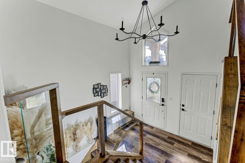 Two-story foyer featuring an angular chandelier, wood-finish flooring, and a staircase with glass railings and wood newel posts - 3208 135A Avenue, Edmonton, AB - Indoor Photo Showing Other Room