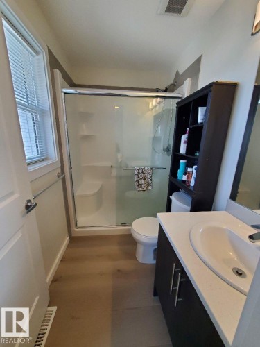 Bathroom featuring wood-finish flooring, a white vanity with an integrated sink, a glass-enclosed shower, and a window with blinds - 118 655 Watt Boulevard, Edmonton, AB - Indoor Photo Showing Bathroom