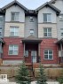 Multi-level townhome featuring a covered entry, horizontal siding in varying shades, dark framed windows, and a tiered wooden retaining wall with planted evergreens - 118 655 Watt Boulevard, Edmonton, AB  - Outdoor 