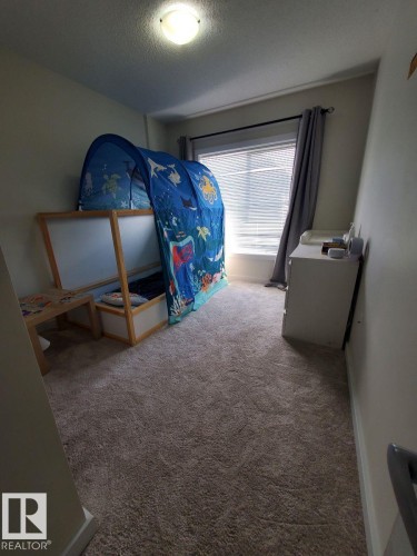 Carpeted interior room featuring a window with horizontal blinds and a ceiling-mounted light fixture - 118 655 Watt Boulevard, Edmonton, AB - Indoor
