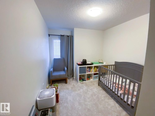 Light gray carpeted room featuring a single window with blinds and gray curtains, light-colored walls, and a ceiling-mounted light fixture - 118 655 Watt Boulevard, Edmonton, AB - Indoor Photo Showing Bedroom