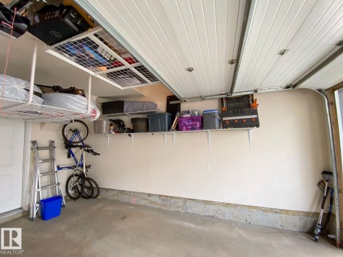 Garage interior featuring an overhead storage rack, wall-mounted shelving, concrete flooring, and a sectional garage door - 118 655 Watt Boulevard, Edmonton, AB - Indoor Photo Showing Garage