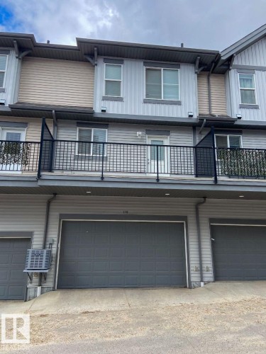 Three-story townhouse exterior featuring a two-car garage with a dark gray door, a second-story balcony with black metal railing, and horizontal siding in light gray and beige tones - 118 655 Watt Boulevard, Edmonton, AB - Outdoor With Exterior