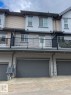 Three-story townhouse exterior featuring a two-car garage with a dark gray door, a second-story balcony with black metal railing, and horizontal siding in light gray and beige tones - 118 655 Watt Boulevard, Edmonton, AB  - Outdoor With Exterior 