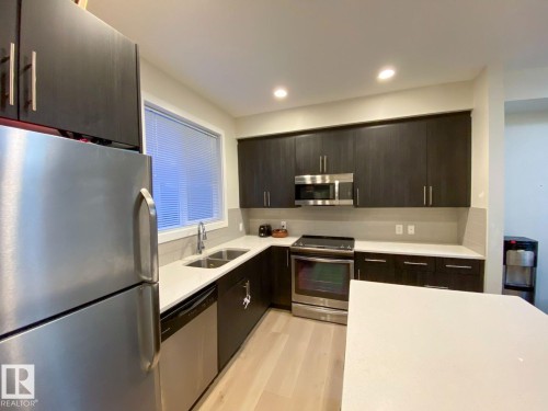 Kitchen featuring dark wood-finish cabinetry, stainless steel appliances, a double basin sink, and light countertops - 118 655 Watt Boulevard, Edmonton, AB - Indoor Photo Showing Kitchen With Double Sink With Upgraded Kitchen