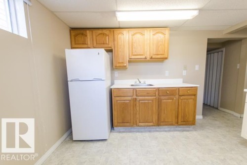 The property features a kitchen area with wood cabinetry, a white countertop, and a white refrigerator - 10806 64 Avenue, Edmonton, AB - Indoor Photo Showing Kitchen