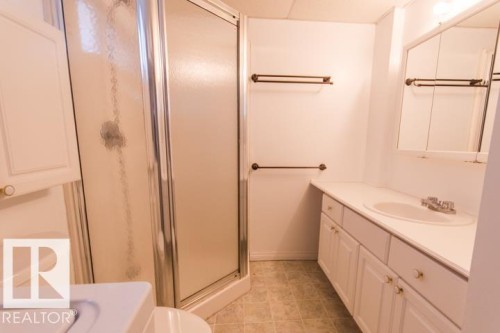 The bathroom features a standing shower with a clear and frosted glass enclosure, a vanity with a white countertop and integrated sink, and a mirrored medicine cabinet - 10806 64 Avenue, Edmonton, AB - Indoor Photo Showing Bathroom