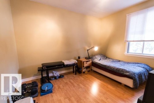 A room featuring light-colored walls, hardwood flooring, and a window with blinds providing natural light - 10806 64 Avenue, Edmonton, AB - Indoor Photo Showing Bedroom