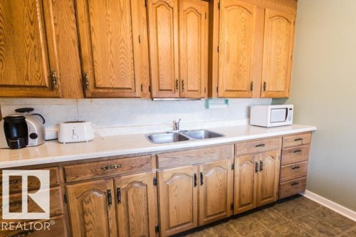 The kitchen features wood cabinetry, a double basin sink, and a white countertop - 10806 64 Avenue, Edmonton, AB - Indoor Photo Showing Kitchen With Double Sink